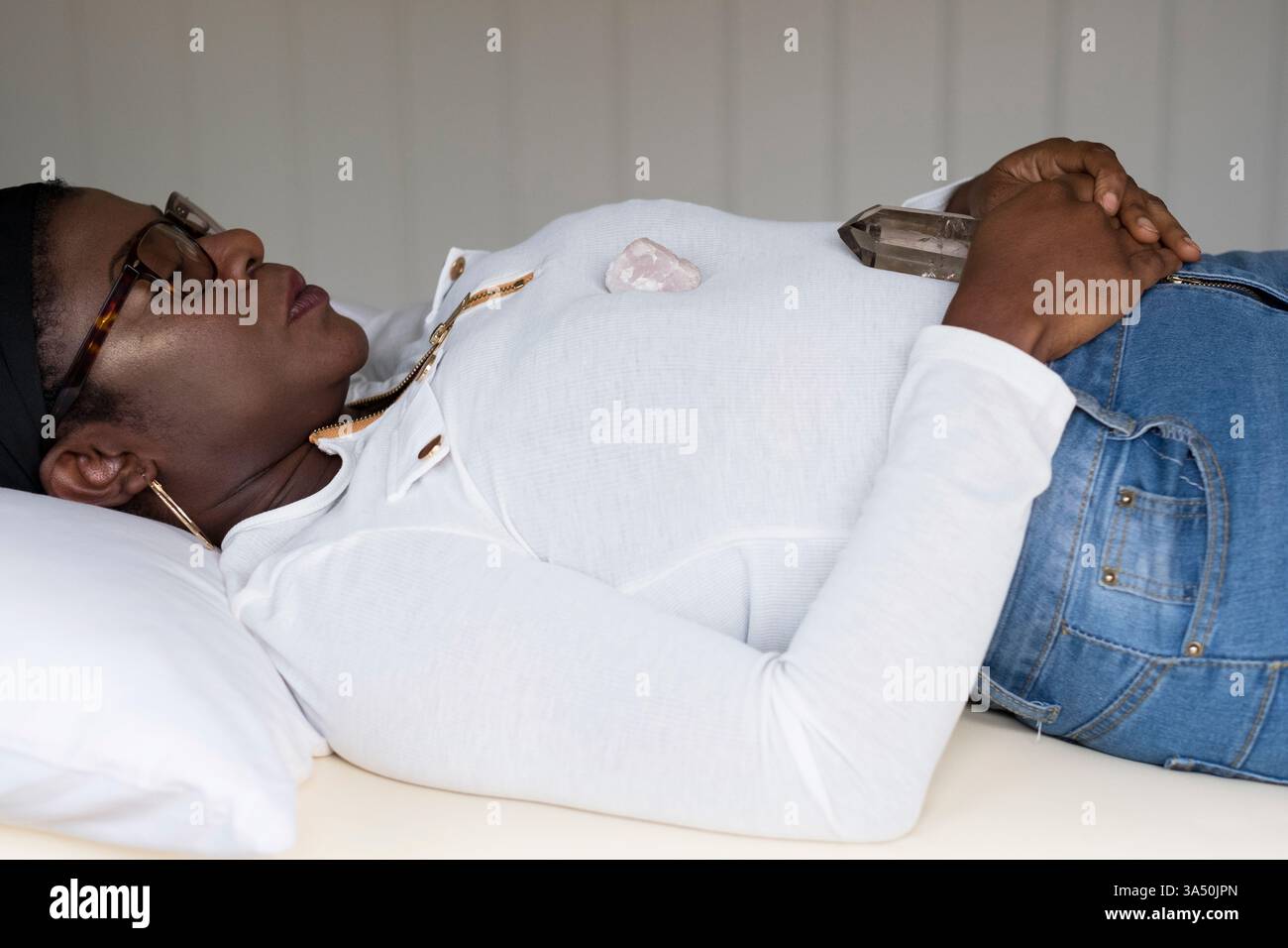 Black woman relaxing during an indoor wellness session with crystals on her chest. Calm, serene mood suitable for wellbeing, mindfulness, and alternative therapies. Stock Photo
