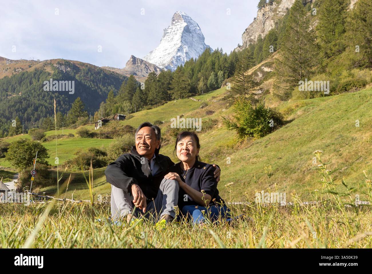 Cheerful Korean couple relaxing in Zermatt, Switzerland with the Matterhorn in the background. Stunning alpine scenery makes this travel image ideal for vacation planning and destination features. Suitable for couples getaways and inspiration photography. Stock Photo