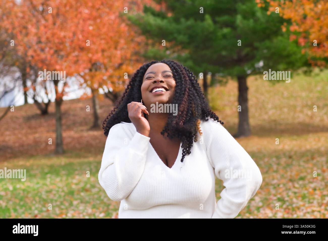 Cheerful Black woman in a park raising her arm and laughing in daylight ...