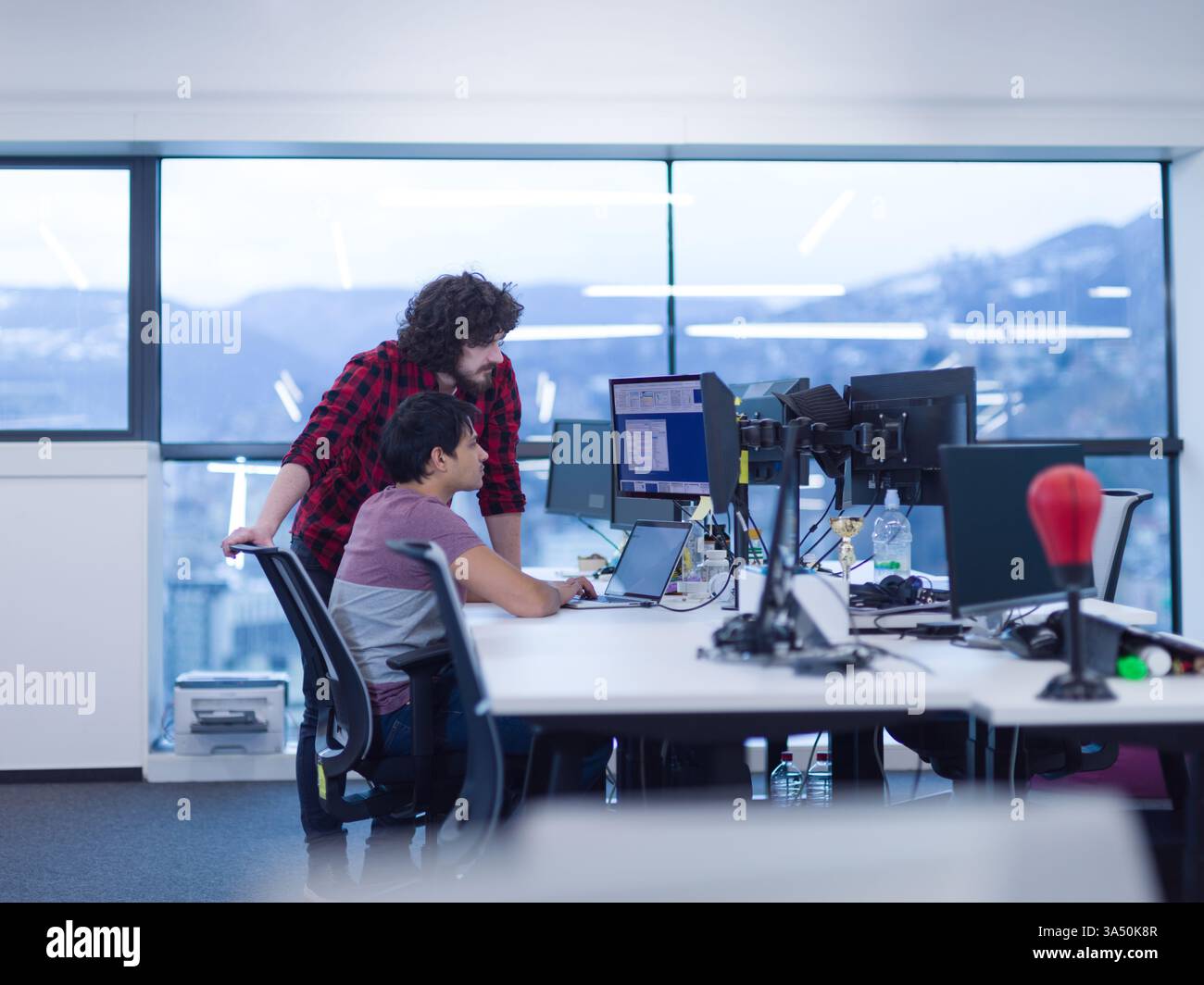 Two young software developers coding at a modern startup office. A contemporary technology and teamwork scene suitable for business, IT, and entrepreneurship themes. Great for articles about coding, startups, and creative workspaces. Stock Photo