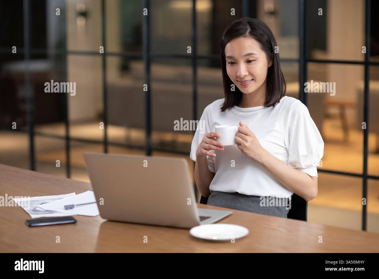 Smiling Chinese businesswoman holding a cup of coffee while looking at ...