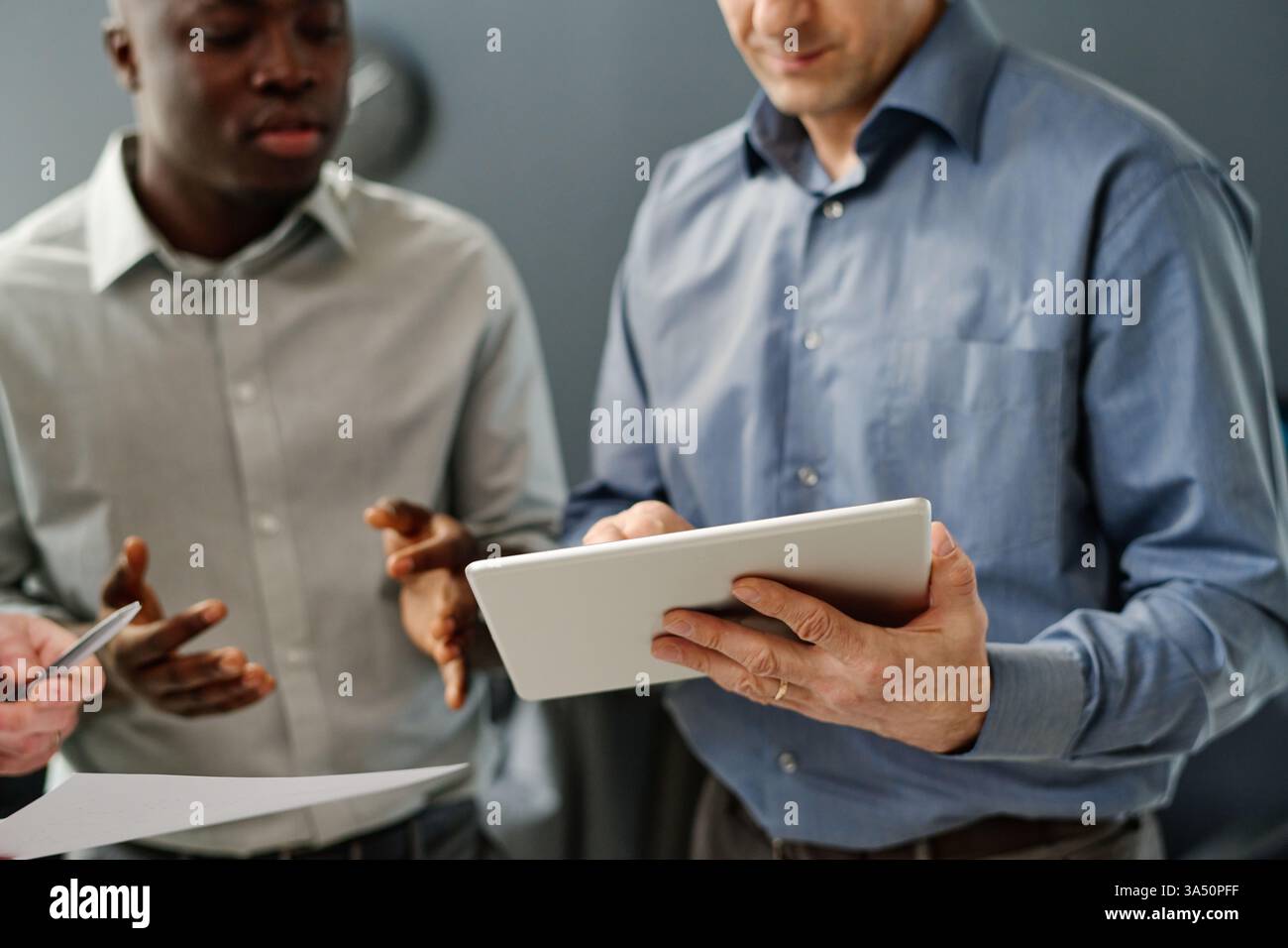 Selective focus image of diverse trading specialists in an office analyzing currency values on a tablet. This finance and business scene is ideal for stock market, fintech, and corporate communications visuals. Great for articles on currency trends, investment strategies, and teamwork. Stock Photo