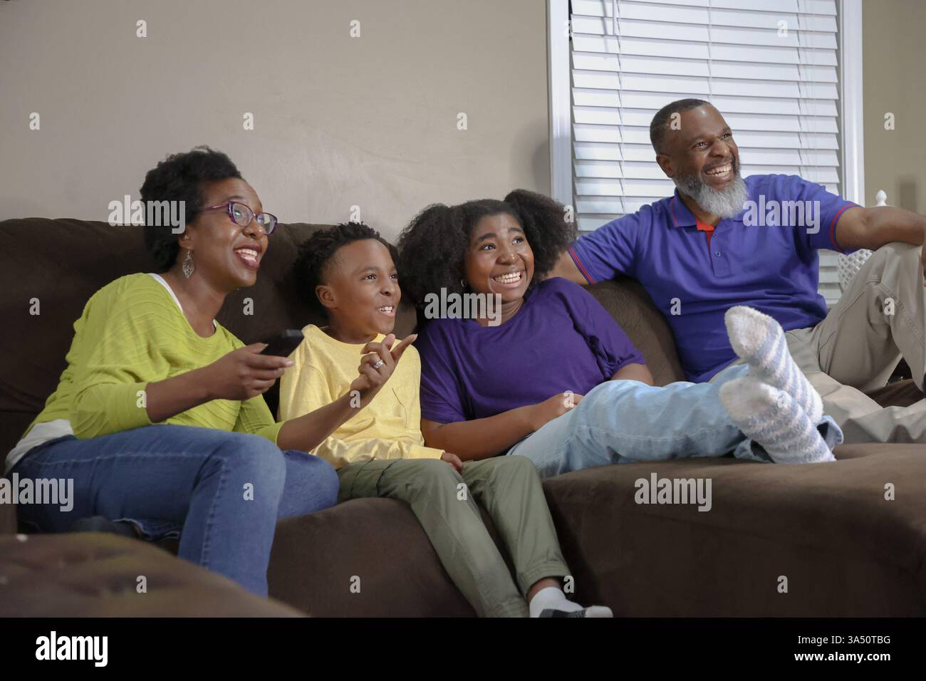 Cheerful Black family sitting together on a brown couch watching TV in ...
