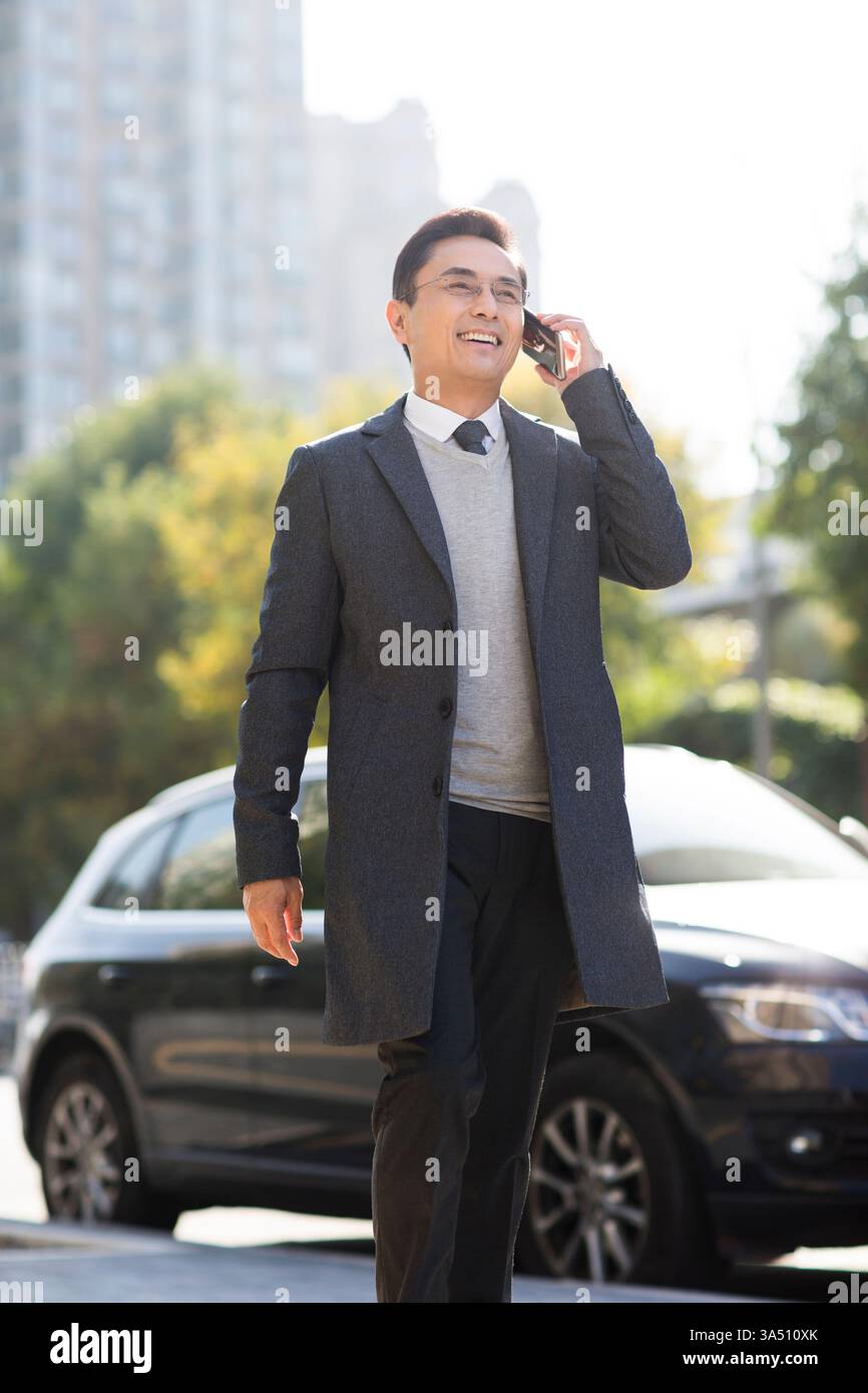 Daytime Phone Example Smiling Chinese businessman on a daytime phone call walks along a city ...