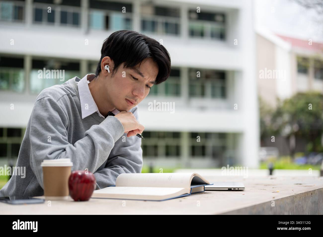 Focused Asian male student sitting reading book with face on hand ...