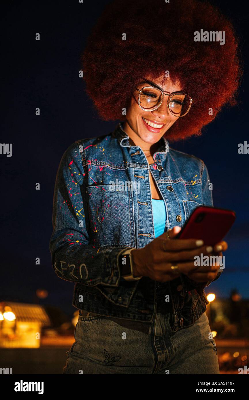 Black woman with afro hairstyle using cellphone standing on street at ...