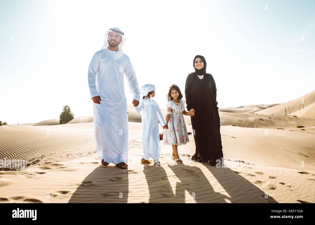 Arab family holding hands and walking together in a desert at sunset. A ...