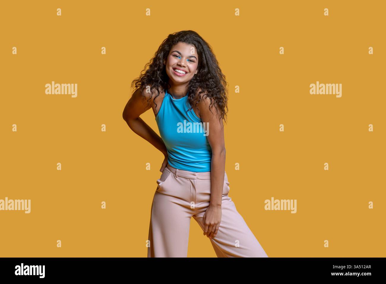 Smiling African American woman stands with one hand on her hip against a bright yellow backdrop. This studio shot works well for fashion, lifestyle branding, and positive-ambition campaigns. Stock Photo