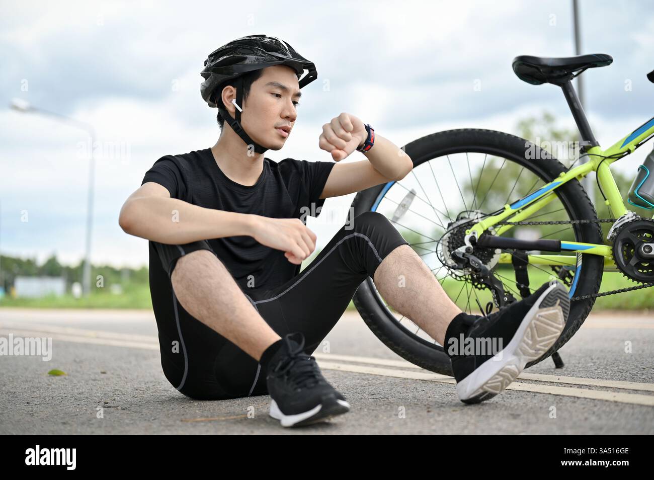 A tired young Asian male cyclist sitting on the street with his bike ...