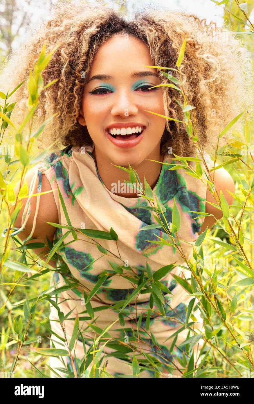 Ethnic young woman with curly blonde hair stands amidst tall green ...