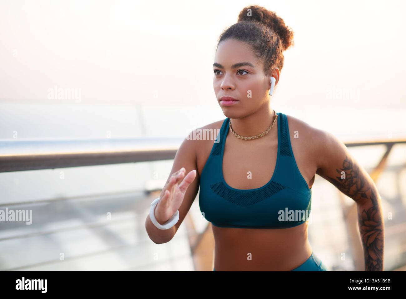 African American woman running outdoors in bright summer weather, listening to music with earphones. The image captures a healthy lifestyle moment during a solo jog. Perfect for fitness, training, and motivation content. Stock Photo