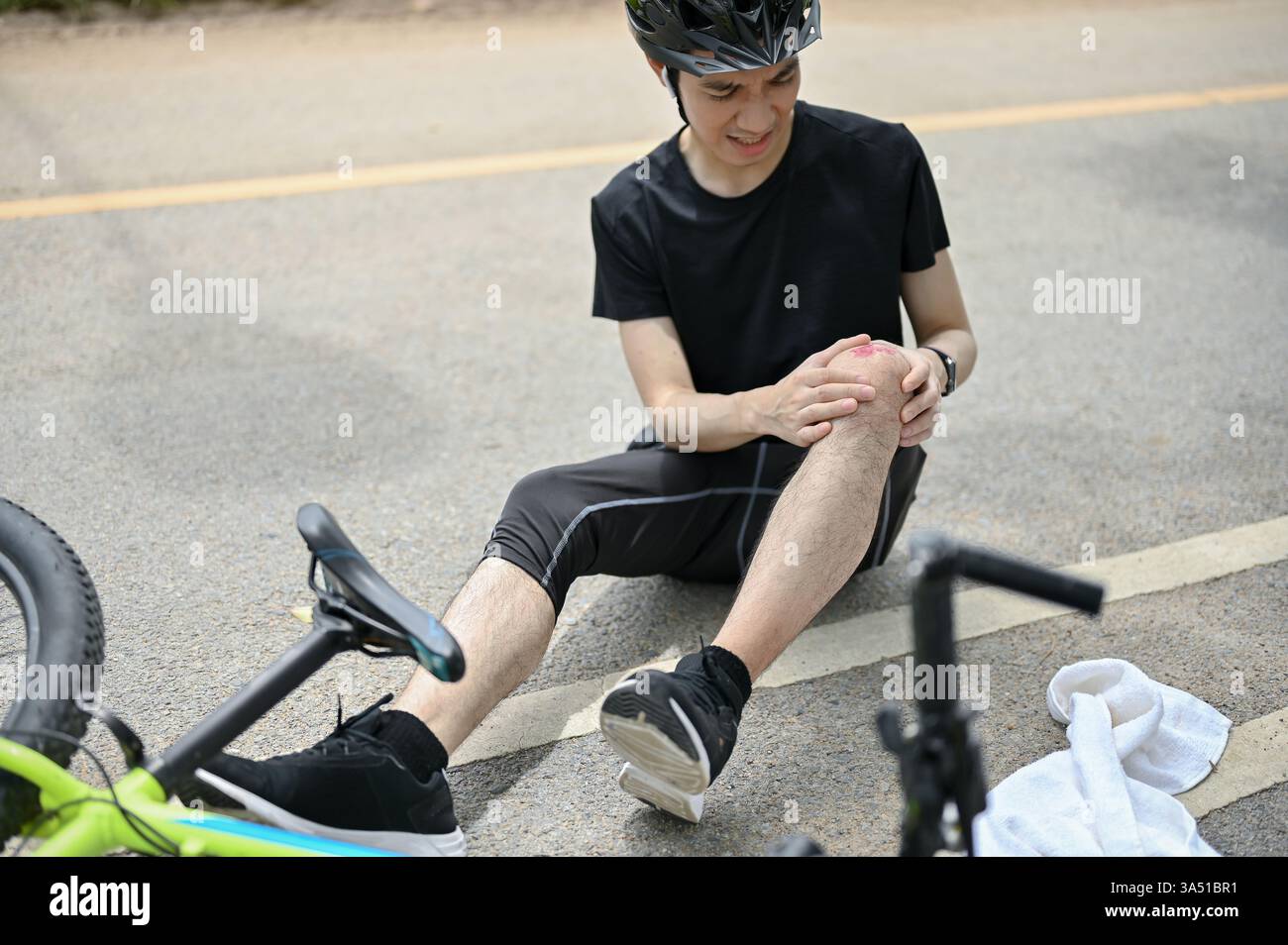 An injured young Asian male cyclist in sportswear and a helmet has ...