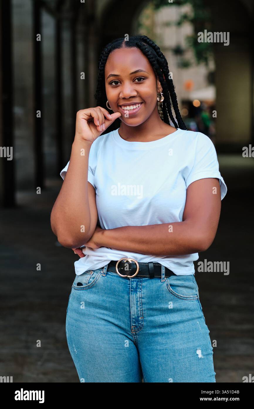 Smiling Black woman with long braids in a white shirt stands outdoors ...