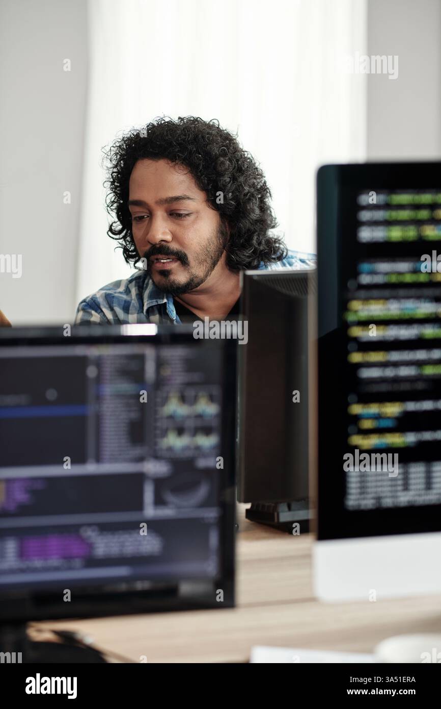 Indian software developer coding on a computer in a modern office. Focused on a screen, this image conveys tech, programming, and software development in a corporate environment. Ideal for IT, technology, and digital workplace themes. Stock Photo