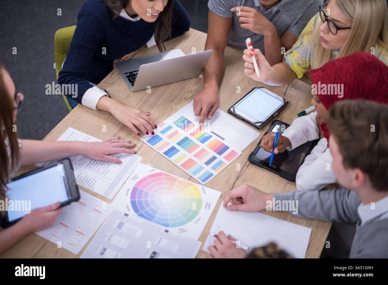 Diverse startup team working on laptops and tablets around a table ...