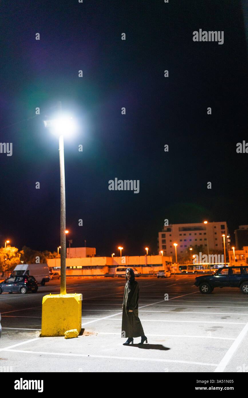 Middle Eastern woman walking through a dimly lit parking lot at night ...