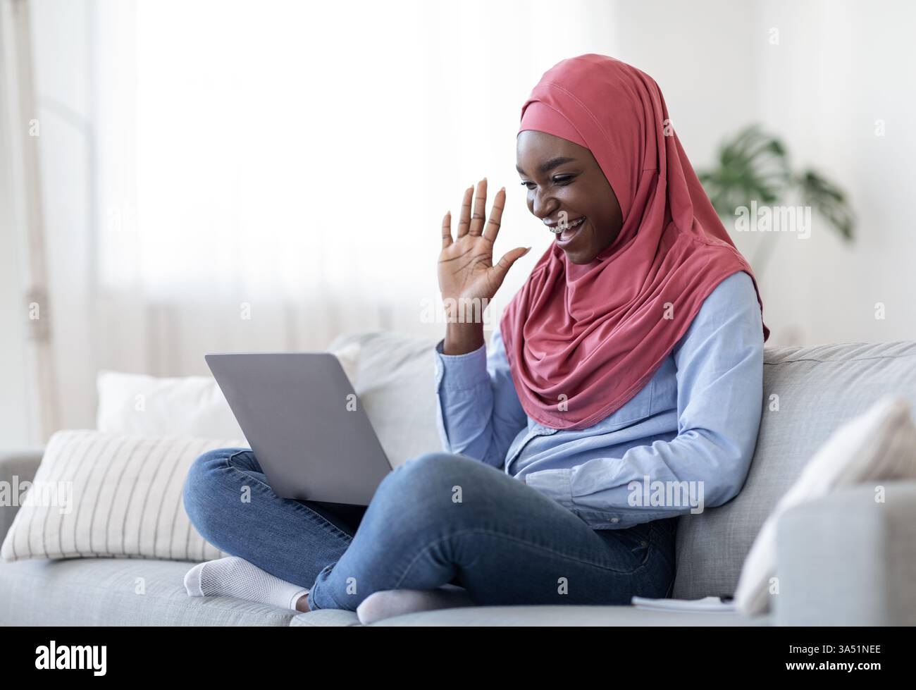 Cheerful black muslim lady in hijab making video call on laptop at home ...