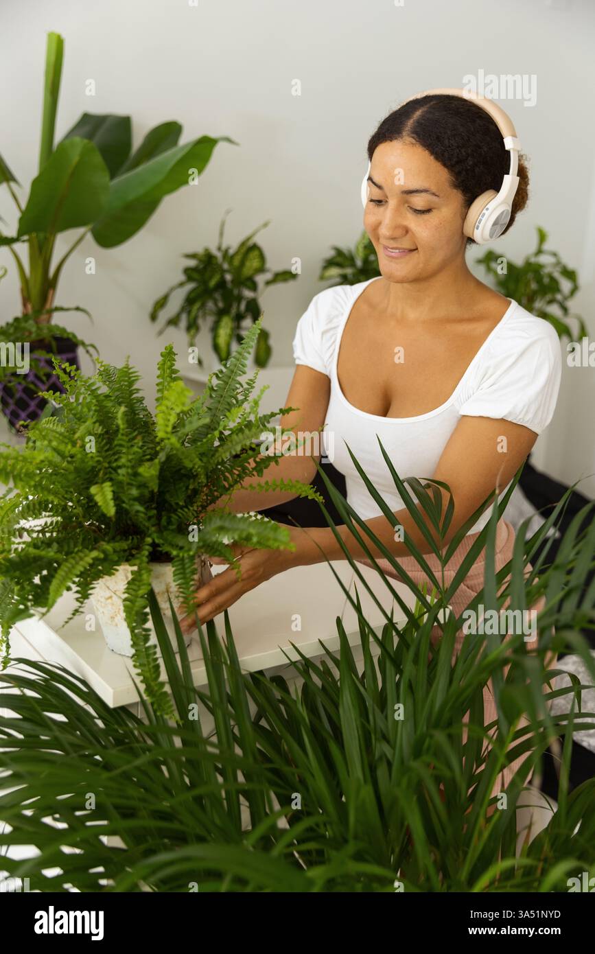 Hispanic female listening to music with headphones while moving potted ...