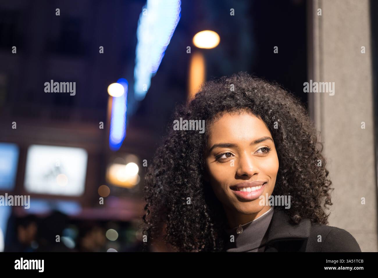 Smiling Black woman looking away standing on city street at night Stock ...