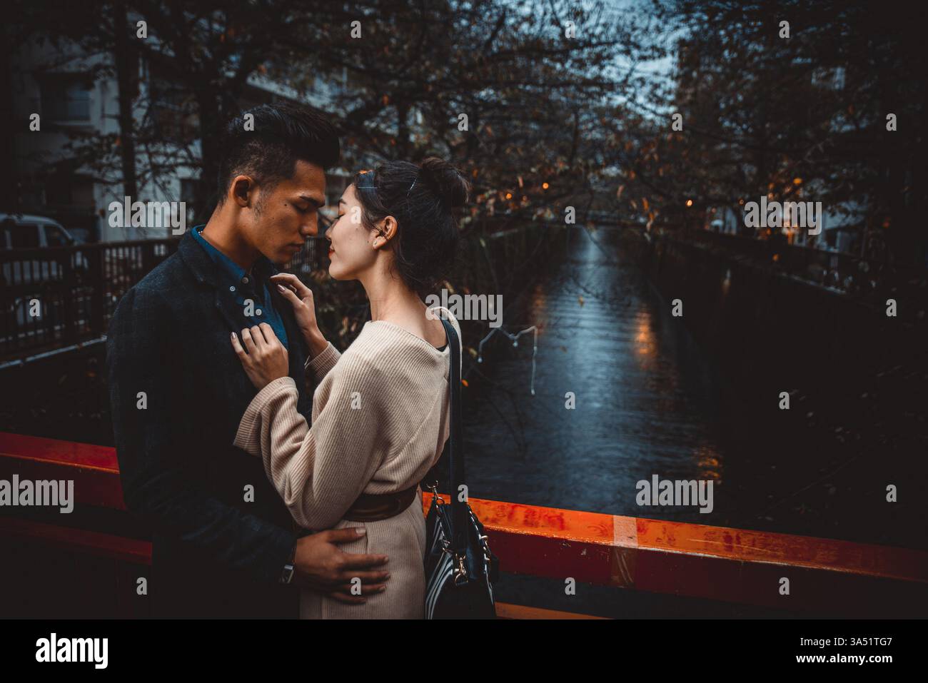 Asian couple with closed eyes kissing while standing on bridge in park at night Stock Photo