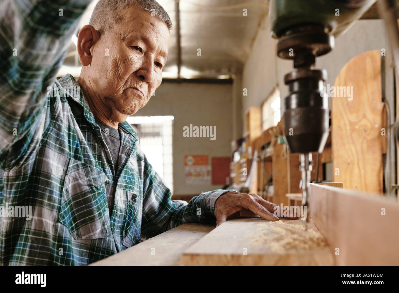 Elderly Asian carpenter using drilling machine to cut clean holes in ...