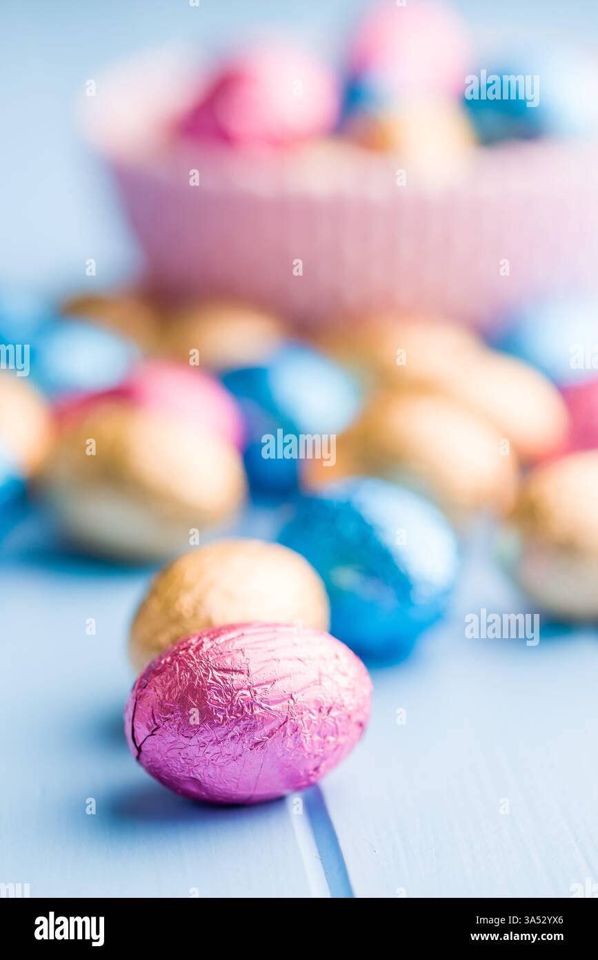 Chocolate easter eggs wrapped in multi colored foil on a blue table. Stock Photo