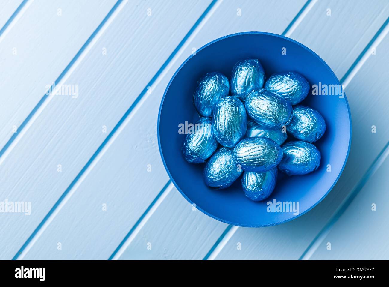 Chocolate easter eggs wrapped in blue colored foil on a blue table. Stock Photo