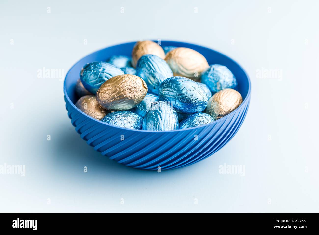 Chocolate easter eggs wrapped in multi colored foil on a blue background. Stock Photo