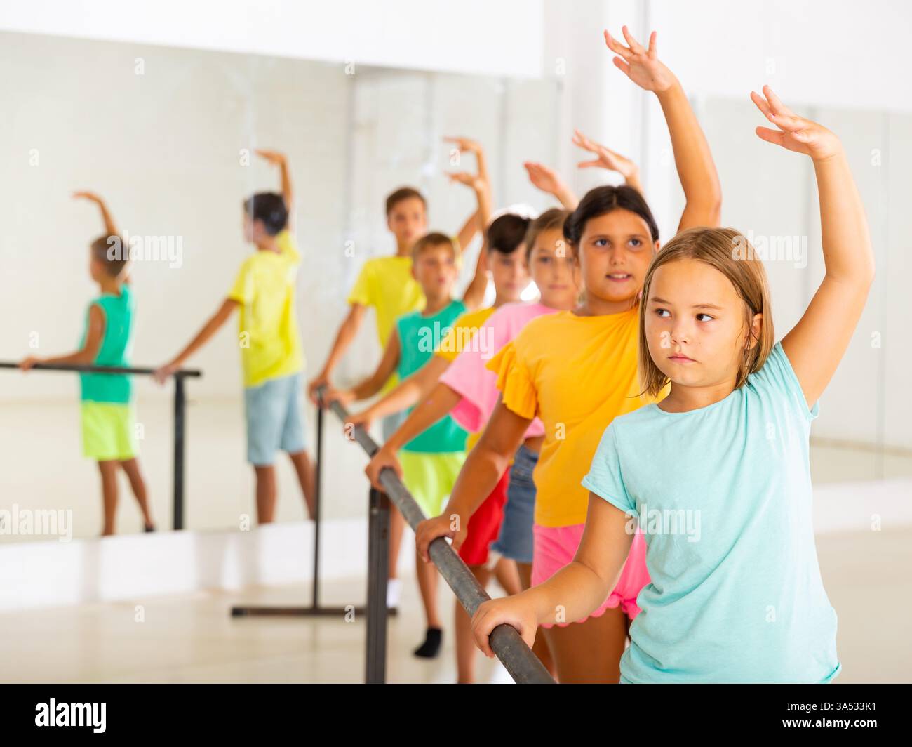 Focused tween girl practicing ballet positions near bar during group class Stock Photo