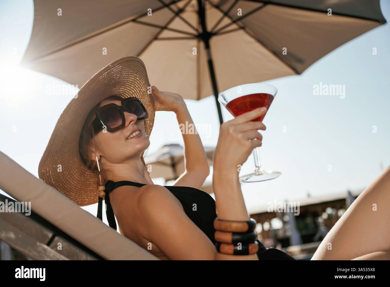 Side view, lying down with cocktail in hand. Beautiful young woman is at resort, vacation. Stock Photo