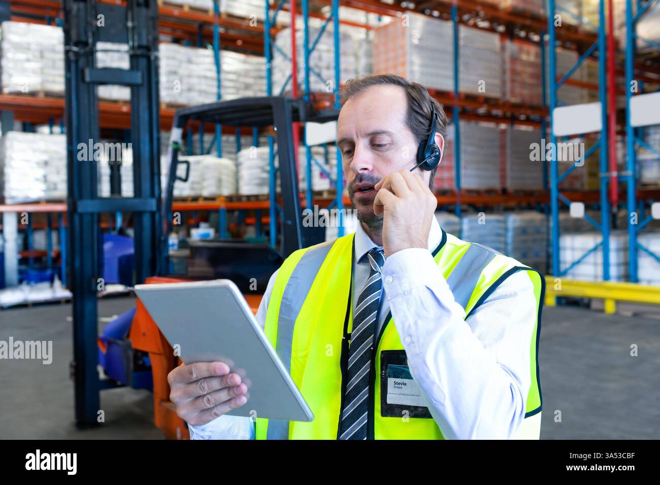 Using tablet and headset, warehouse manager managing inventory and communicating Stock Photo