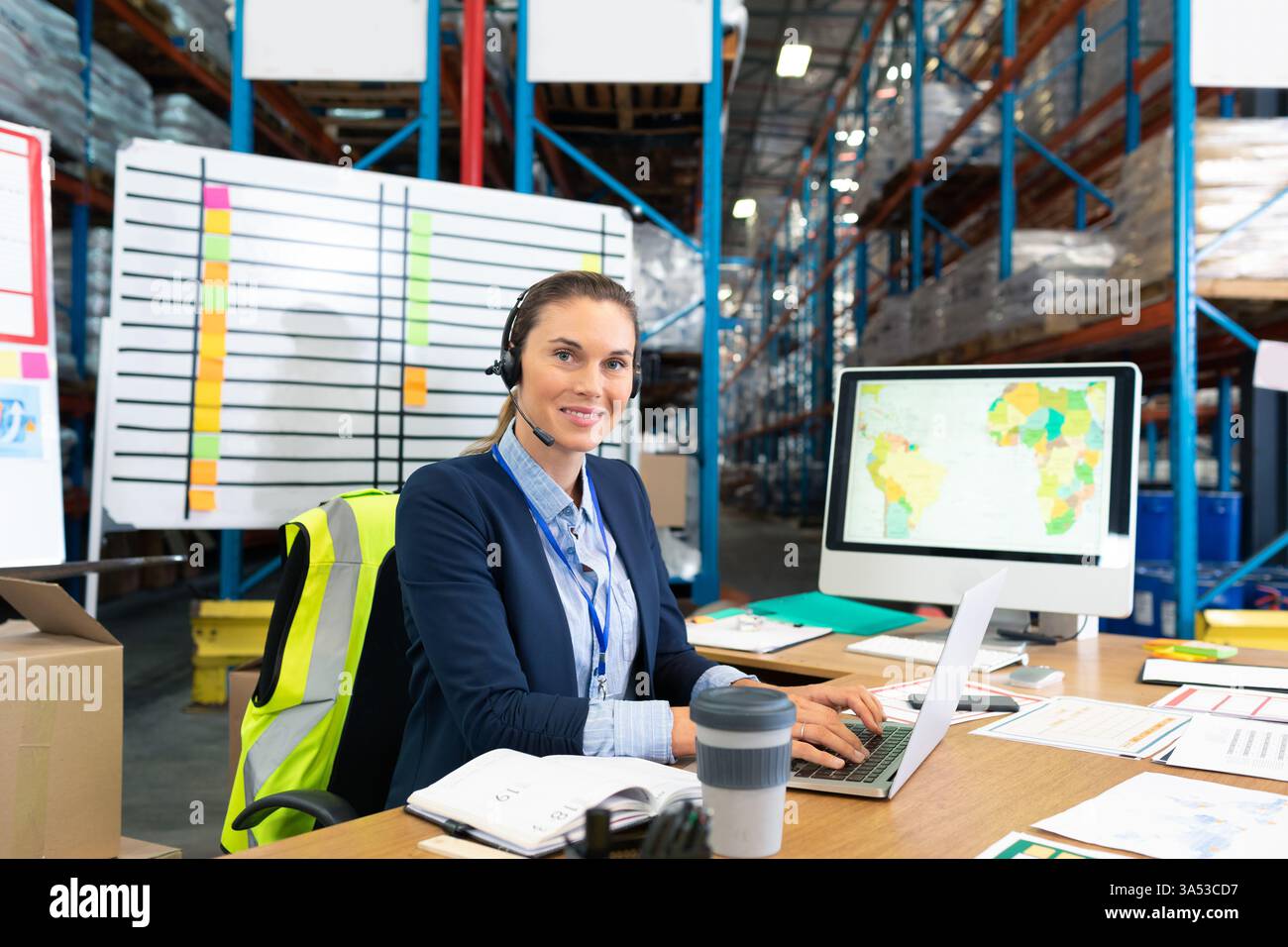 Using computer and headset, warehouse manager coordinating logistics efficiently, copy space Stock Photo
