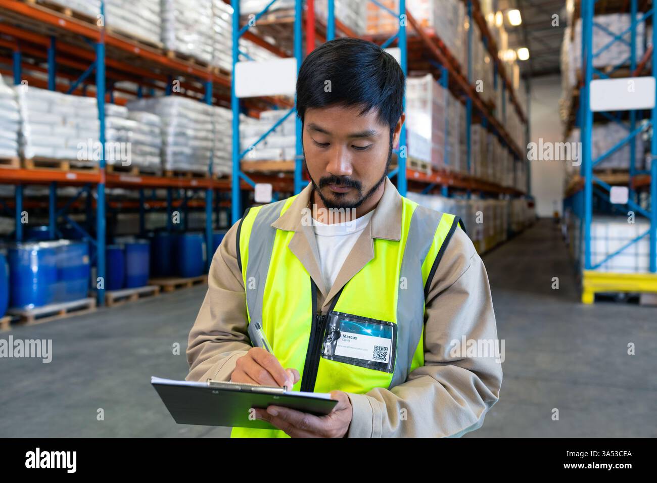 In warehouse, worker in high-visibility vest checking inventory using clipboard Stock Photo