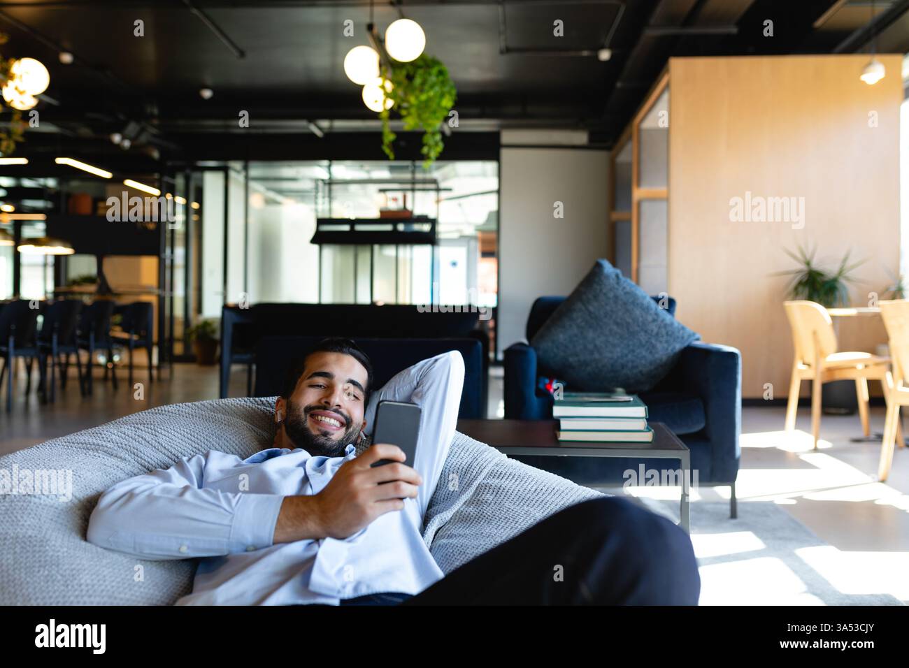 Relaxing in modern office, man smiling while using smartphone on bean bag Stock Photo