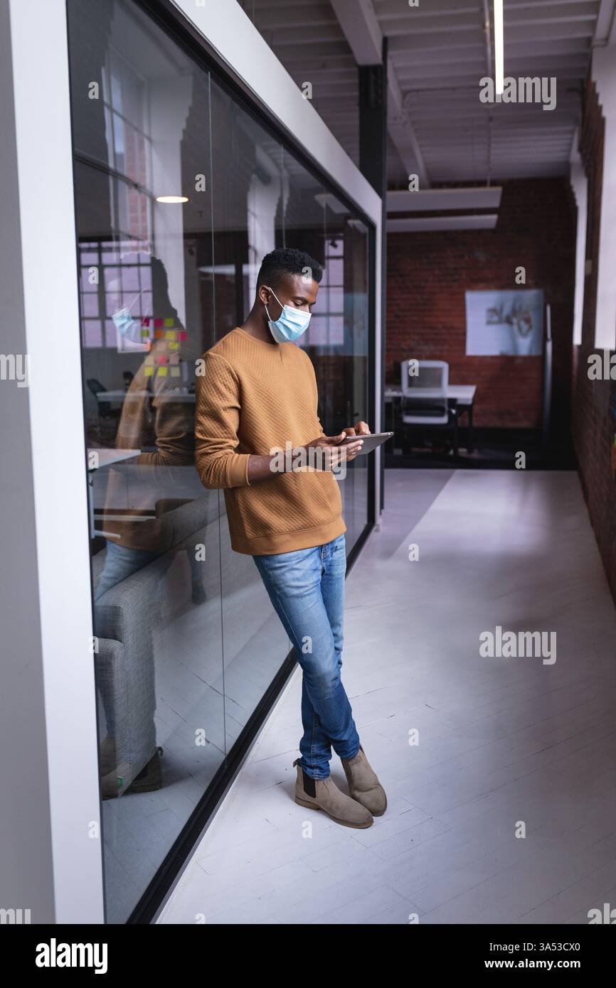 African American man using tablet in modern office, wearing protective face mask Stock Photo