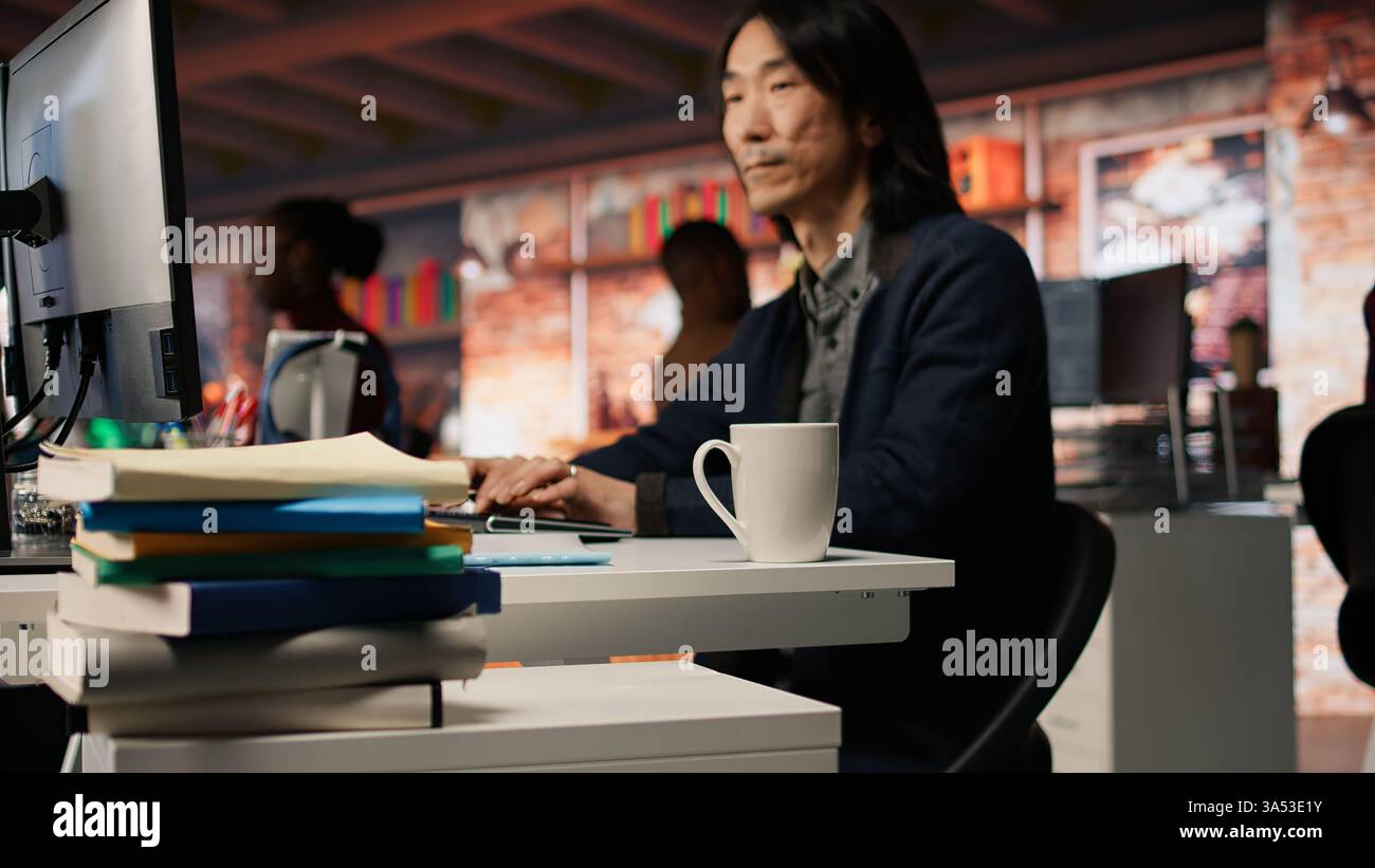 Senior engineer coding advanced AI algorithm in startup office, refining machine learning models to enhance automation. Asian CTO manager using coding platform in Silicon Valley workplace, camera A Stock Photo