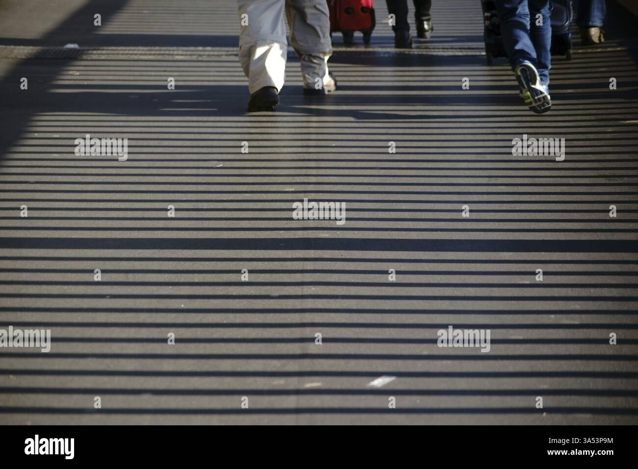 A bridge railing casts striped symmetrical shadows on a pavement Stock Photo