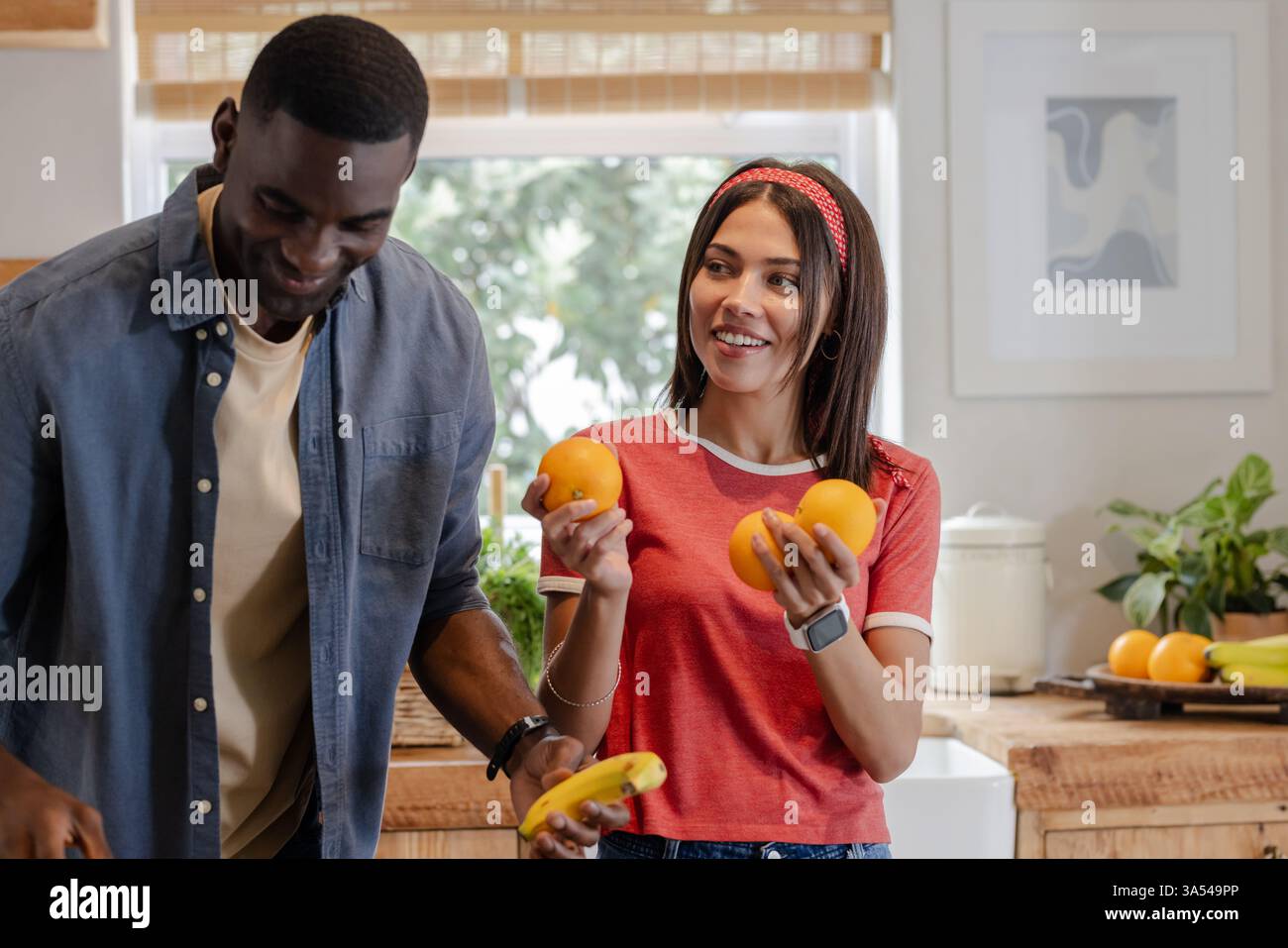 Smiling Diverse couple in kitchen preparing fresh fruit, enjoying time together Stock Photo