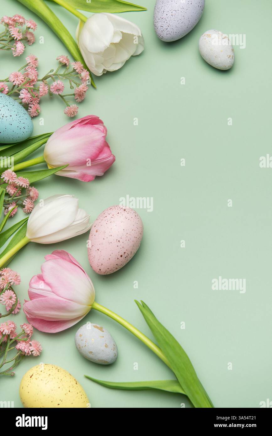 Colorful easter eggs and tulips creating a border on a pastel green ...