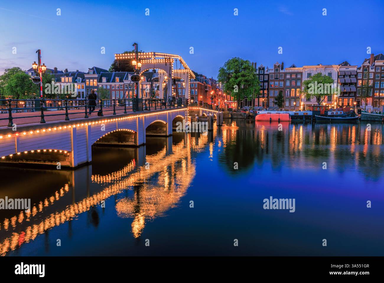 Amsterdam by night in Holland with bright city lights with its canals and old waterfront houses and bridges - a travel image Stock Photo