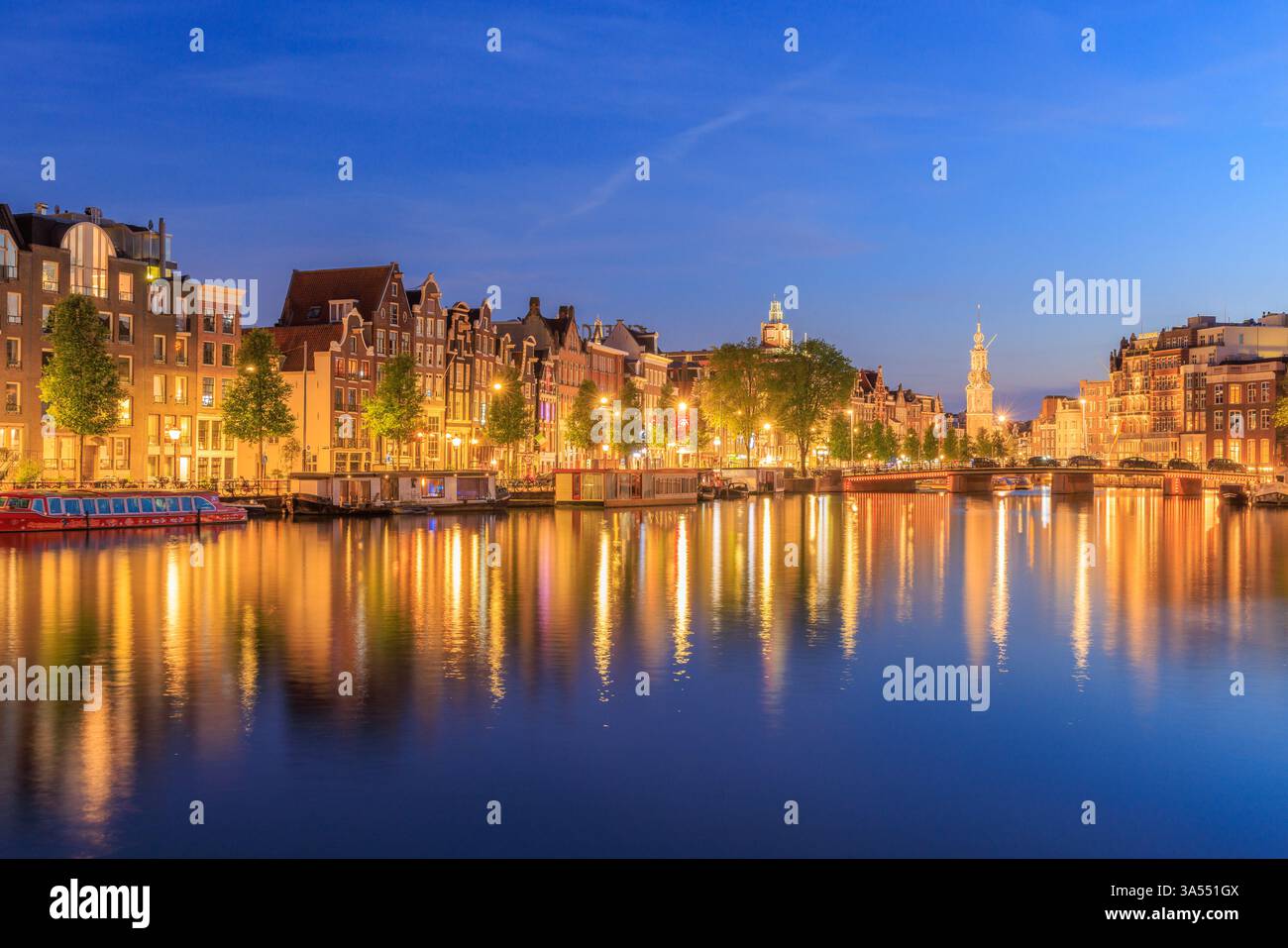 Amsterdam by night in Holland with bright city lights with its canals and old waterfront houses and bridges - a travel image Stock Photo