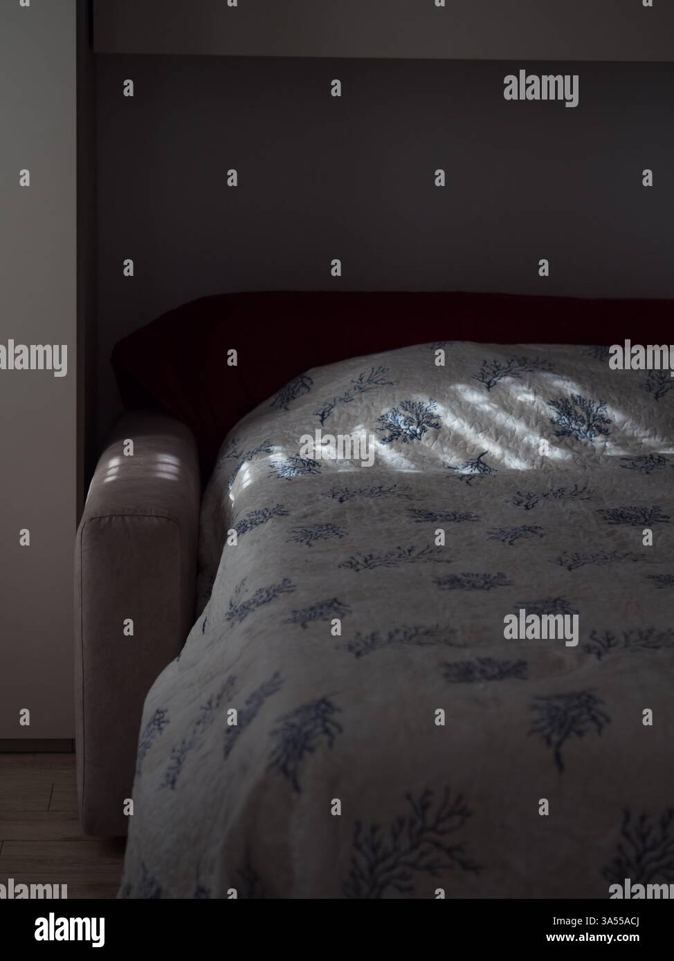 Sunlit Shutter Patterns Cast on a Bed with Coastal Print Blanket Stock Photo