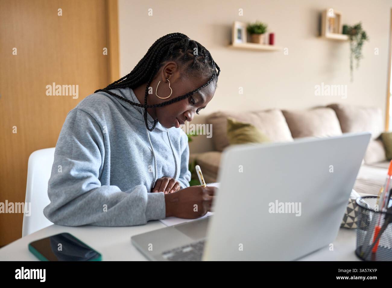 Focused student taking notes while studying online at home Stock Photo
