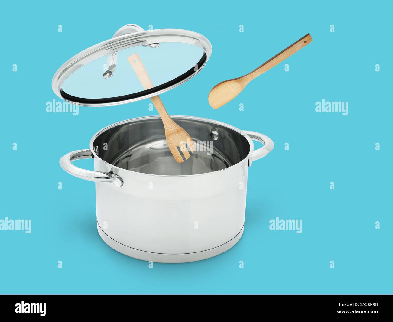 Wooden spoon and turner in air over saucepan on light blue background ...