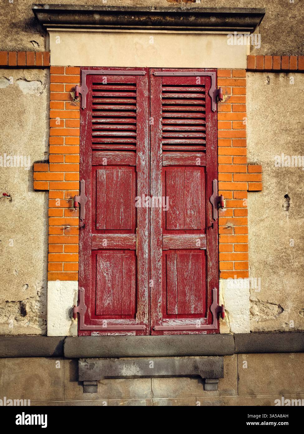 Weathered red wooden shutters are mounted on a crumbling wall with orange bricks, highlighting a blend of colors and textures in an aged urban environ - Smartphone Captured Stock Image