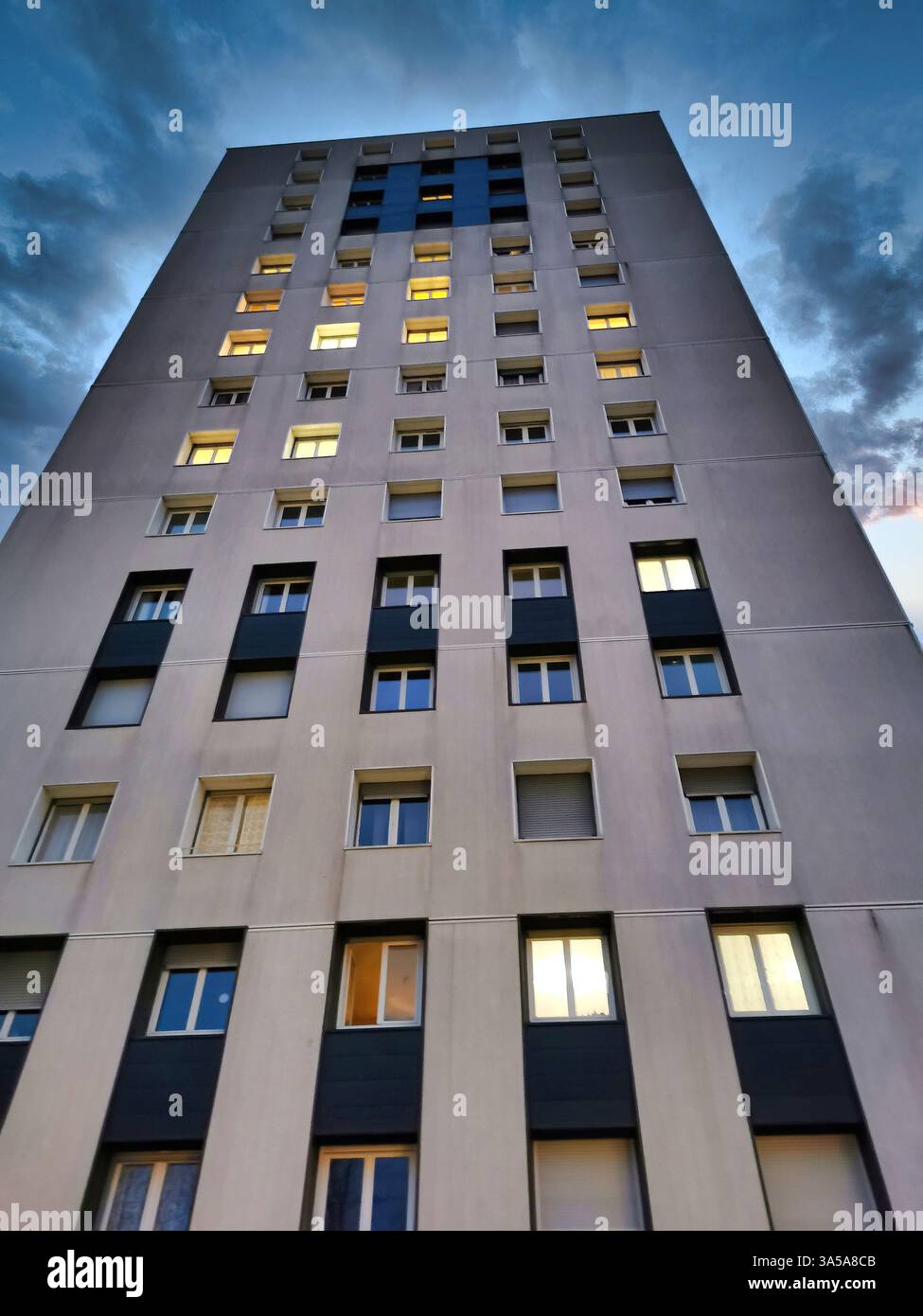 Modern apartment building illuminated at dusk under a dramatic sky with scattered clouds in an urban environment - Smartphone Captured Stock Image