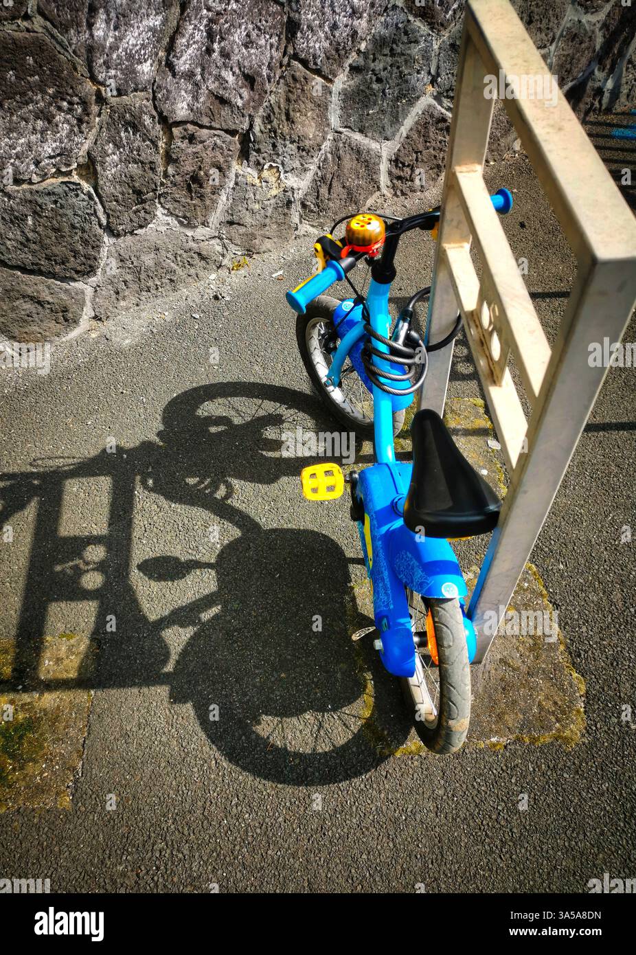 A vibrant blue child's bicycle is parked securely between two metal bike racks on a stone wall-lined street. - Smartphone Captured Stock Image