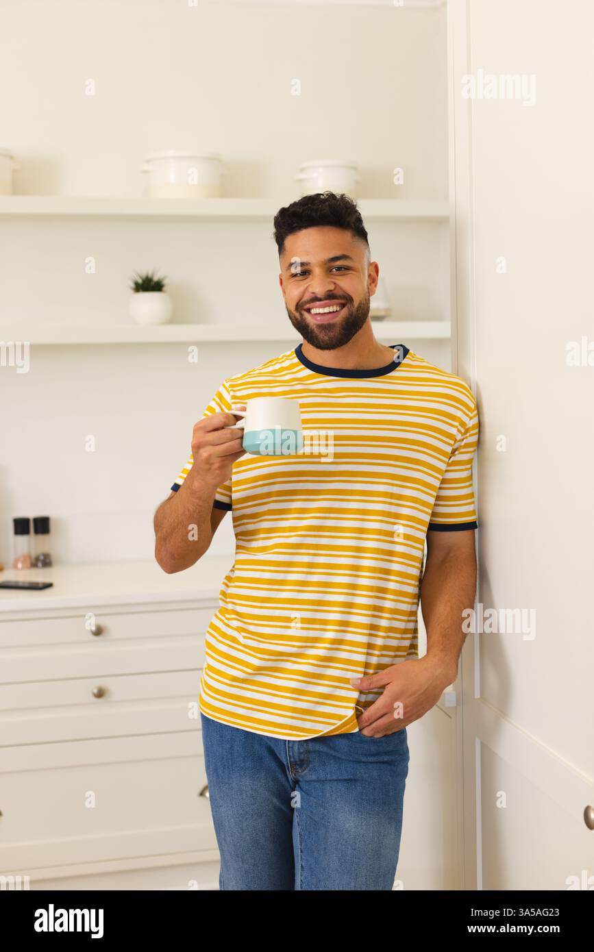 Smiling man in striped shirt enjoying coffee at home in modern kitchen Stock Photo
