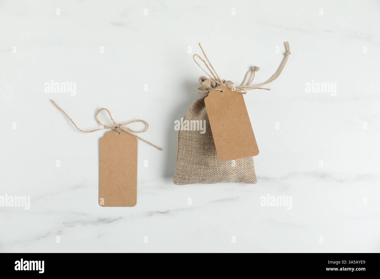 Burlap bag with tags on white marble table, flat lay Stock Photo