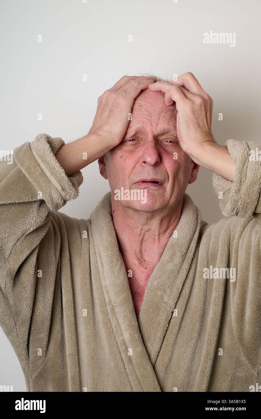 Old man beige bathrobe and tousled hair make a ugly face in front of camera Stock Photo
